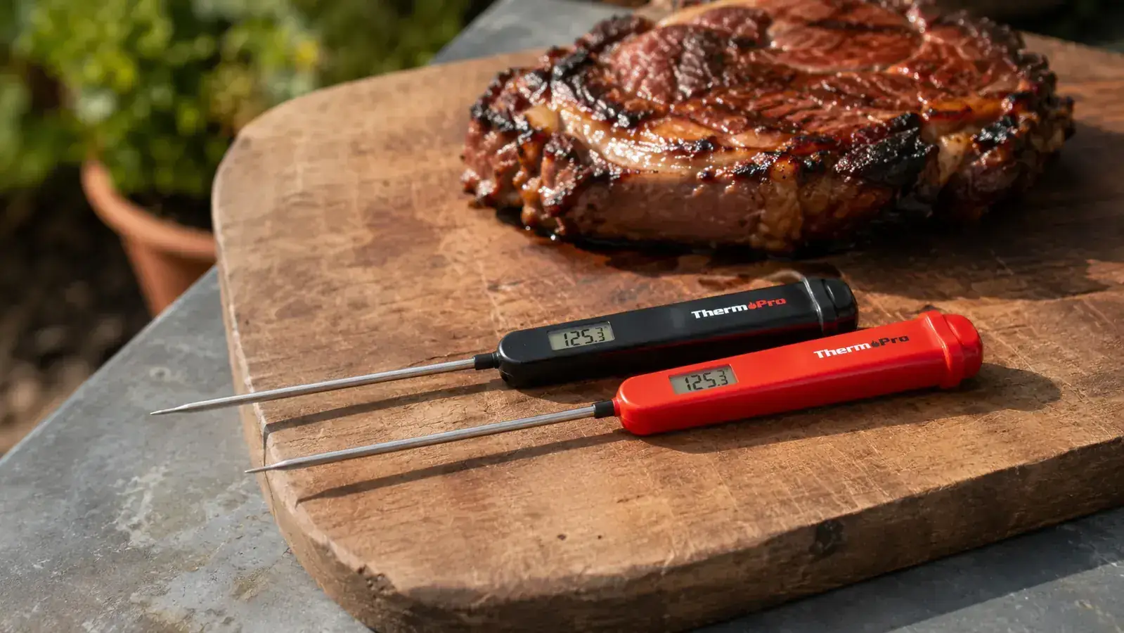 Two instant-read meat thermometers side by side on a wooden cutting board next to a grilled steak