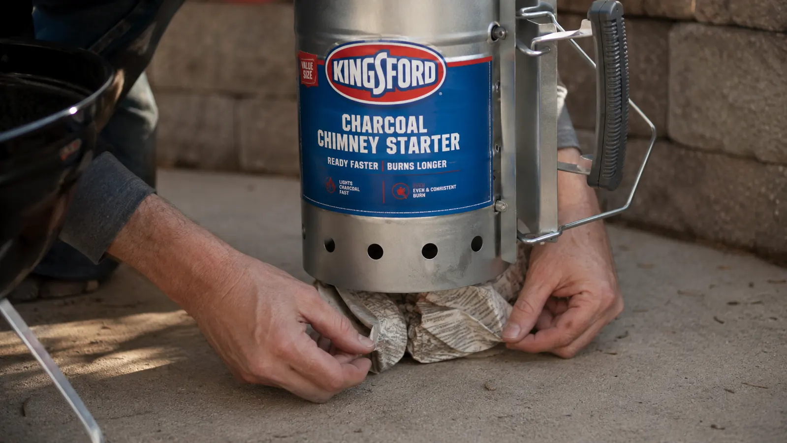 Hand crumpling newspaper and placing it under a Kingsford chimney starter