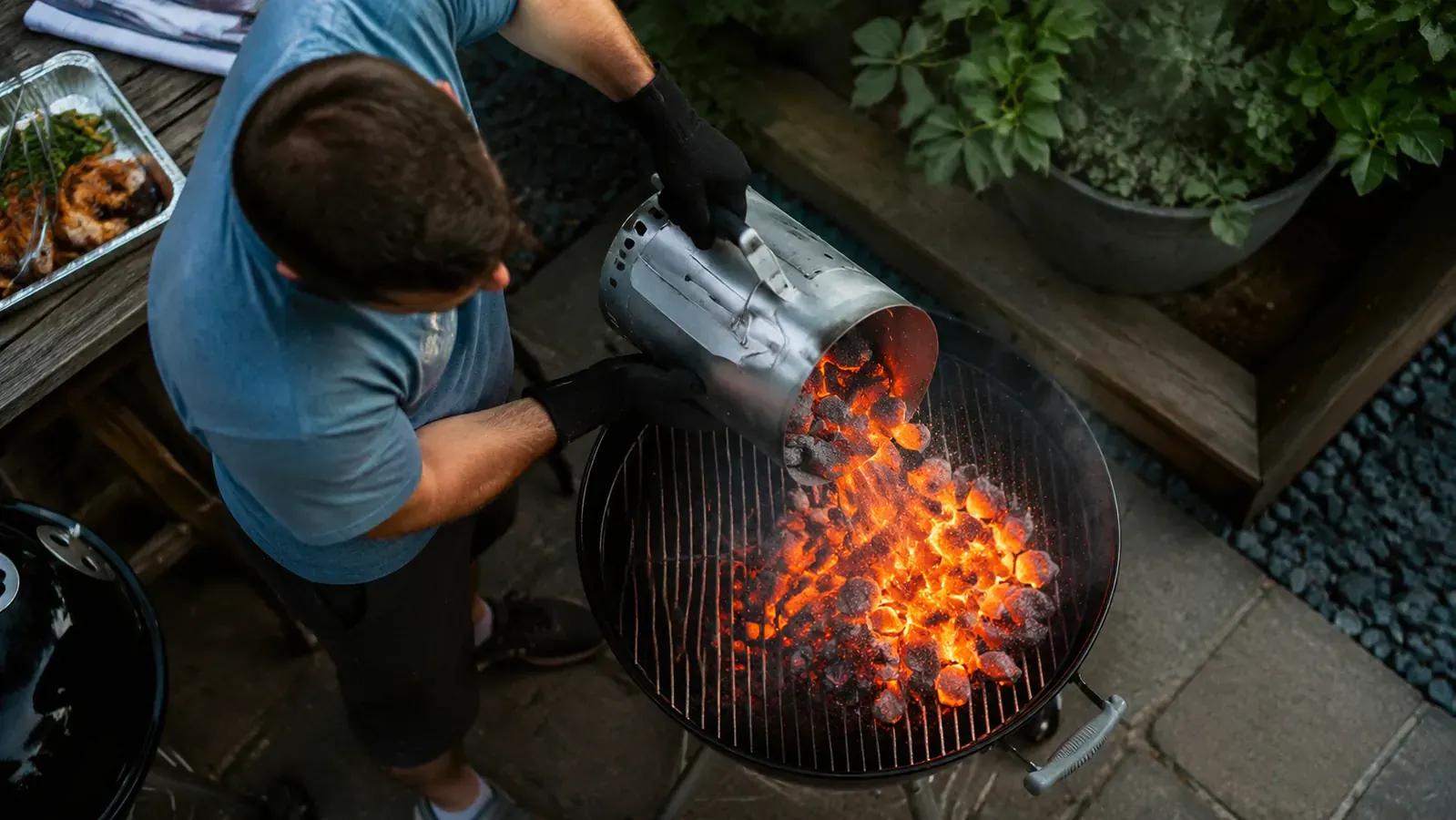 Coals being poured from a chimney starter into the bottom of a charcoal grill, glowing orange