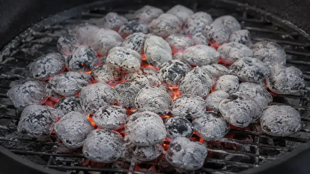 Perfectly ashed-over charcoal coals spread evenly across a kettle grill ready for cooking, no lighter fluid smell