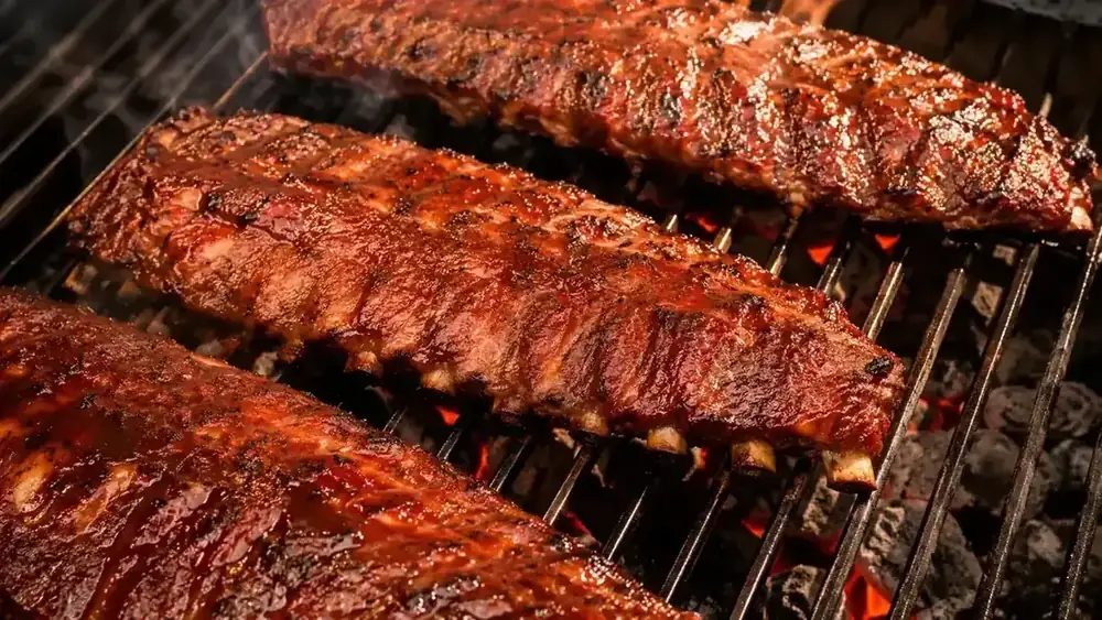 Rack of baby back ribs on a charcoal grill, glistening with fresh BBQ sauce in late afternoon light
